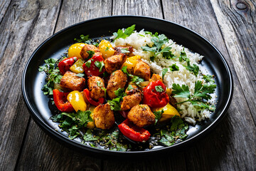 Fried chicken nuggets with white rice, bell peppers and parsley on wooden table