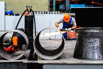 Production of parts from steel pipes of various shapes in an industrial enterprise. Metal blanks on the background of a worker with a grinding machine. Unrecognizable person
