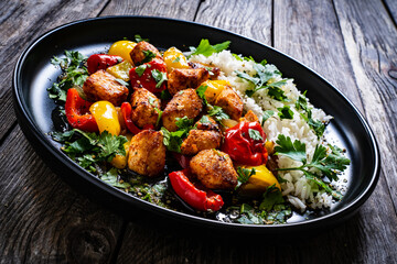 Fried chicken nuggets with white rice, bell peppers and parsley on wooden table