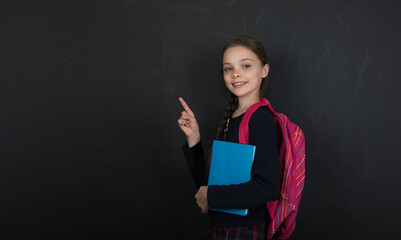 Happy cute child girl  holding books. Smilling schoolgirl   front of black chalkboard.