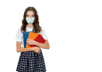 Happy teenager student girl in protective face mask and school uniform holds books. Schoolgirl is going to school in new quarantine reality, isolated on white. Concept of back to school and epidemic