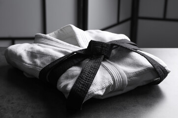 Martial arts uniform with black belt on grey stone table indoors - obrazy, fototapety, plakaty