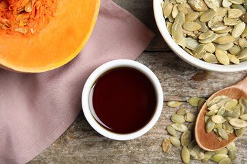 Bowl of oil and pumpkin seeds on wooden table, flat lay