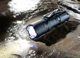 Waterproof tactical flashlight on a rock - obrazy, fototapety, plakaty