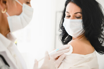 Mature middle-aged patient undergoing injection vaccination against coronavirus Covid 19 wearing protective face mask in hospital