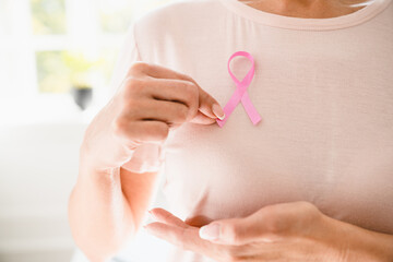 Caucasian woman in pink t-shirt doing palpation with pink ribbon on her breast to support world breast cancer day. Fighting against tumors, recovery from oncology