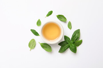 Essential basil oil and fresh leaves on white background, flat lay