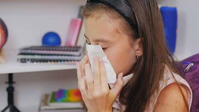 Close-up of a girl blowing her nose on a napkin in the room.