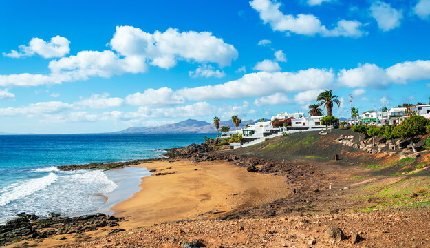 View of Playa El Barranquillo beach in Puerto del Carmen, Lanzarote. Sandy beach with turquoise ocean waves, white houses and mountains, Canary Islands, Spain