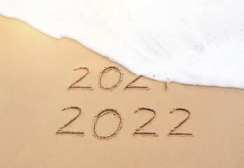 Goodbye 2021 Happy New Year 2022 sign on sandy beach with foam wave. Handwritten 2021 and 2022 on beautiful sand beach. New Years 2022 replace 2021 concept - obrazy, fototapety, plakaty