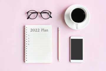 Flat lay of mobile phone, a cup of coffee, glasses and notepad of businesswoman on pink table in office. Business and technology concept top view and copy space.