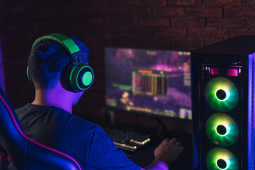 Guy in green headphones playing video games under neon light. © Anastassiya 