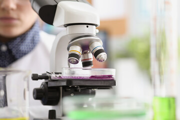 Woman scientist explore purple sample under microscope in laboratory