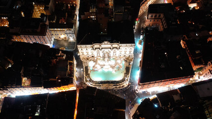 Aerial drone top view night shot of iconic world famous illuminated Trevi fountain or fontana di Trevi in the heart of historic Rome, Italy