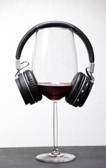 glass of red wine with headphones on leather surface with white background