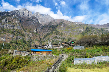 A small cottage on Annapurna Circuit Trek in Himalayas, Nepal. There are mountain chains around the village. Steep and barren slopes. Few prayer flags hanged on the rooftops. Serenity and calmness.