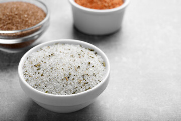 Different kinds of salt in bowls on grey table, space for text