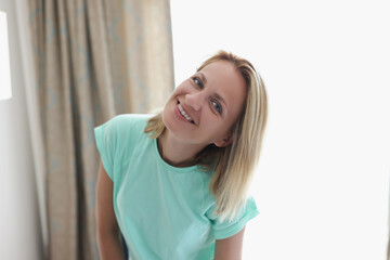 Happy smiling blonde young woman in apartment posing on curtain