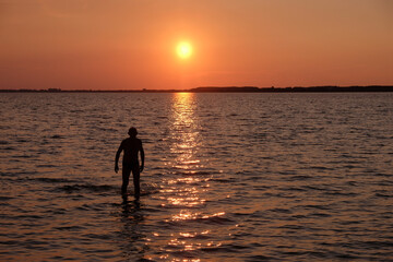 Silhouette of a lonely man walking on the water at sunset on the lake. The sunny path on the water. Copy space. 