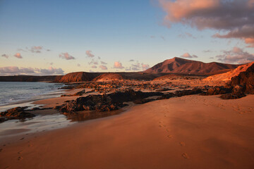 Fototapeta na wymiar The west coast of Lanzarote at a beautiful sunset. A beach and a blue sky with some clouds. View to the mountain range Los Ajaches. Canary Islands, Spain.
