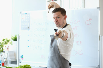 Attractive male chef standing in apron and pretend hes fighter with cooking knife
