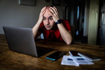 A man with his hands on his head in shock looking at a laptop with passports, a cellphone and covid...