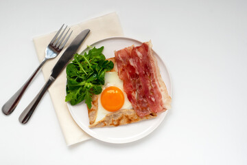 Galette bretonne with fried eggs, arugula and bacon. French pancake made from buckwheat flour with...