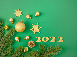 Gold numbers 2022, gold Christmas ornaments, gold snowflake and green Christmas tree branches on green background top view. copy space