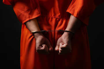 Prisoner in jumpsuit with handcuffs on black background, closeup