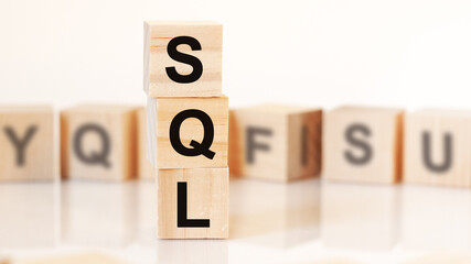 wooden cubes with letters SQL arranged in a vertical pyramid, white background, reflection from the surface of the table. SQL - short for Structured Query Language