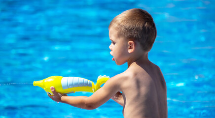 Happy child in the pool playing with a water gun.