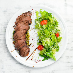Veal steak with salad and vegetables. On a white background. Top view.
