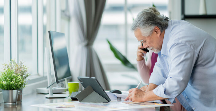asian senior copule working at home,retired old asian male and his wife hand use smartphone discuss with client and check data information with laptop on table in living room at home