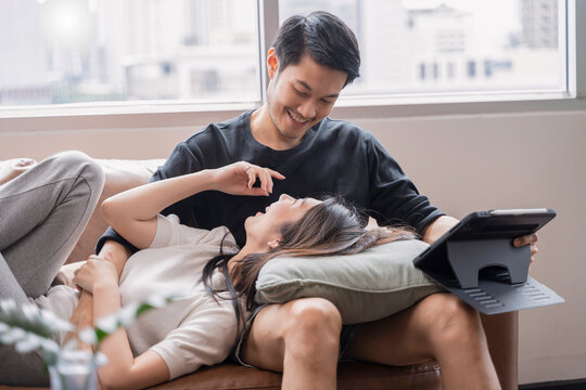 lifestyle at home,asian female stay home together with her husband watch movie online by tablet on sofa in living room at home,sweet asian marry couple spending weekend time together at home