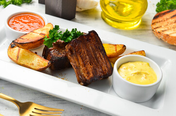 Baked juicy pork ribs with potatoes and sauce. Top view. On a white plate.