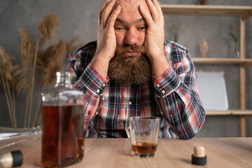 Alcoholism concept. The young man drinks too much alcohol. Sits at home at the table in casual...