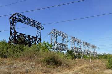 Fototapeta premium Electricity poles and electric power transmission lines. High voltage electric transmission tower. Electrical pylon and high voltage power lines against blue sky. 