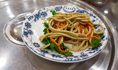 A plate filled with tofu skin and fresh vegetables placed on a white porcelain plate with blue decorations. The dish is served on a metal table. Nutrition and supplementation