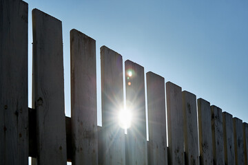 Wooden gray fence on a sunny summer day. The sun shines through the fence