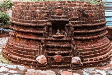 Stara ceglana stupa buddyjska z małym posągiem buddy.