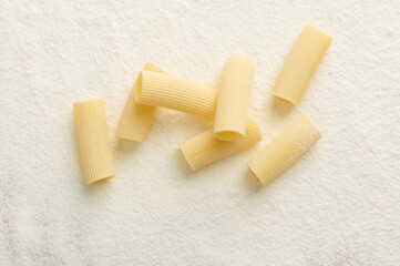 Studio shot with soft shadow of raw Italian pasta- whole wheat tortiglioni on white background with scattered flour. Copy space for food advertisement. Top view