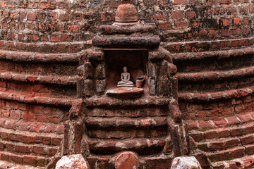 Stara ceglana stupa buddyjska z małym posągiem buddy.