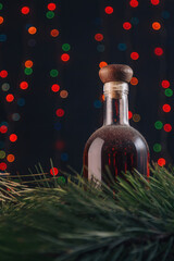 Old cellar dusty bottle of brandy, scotch, whiskey, cognac on blurry Christmas garland lights bokeh background, green pine branches. Vertical shot