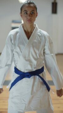 Vertical shot of focused girl showing defending karate poses. Front view of serious fighter in kimono lunging forward and backward, improving skills and exercising in gym. martial arts, sport concept