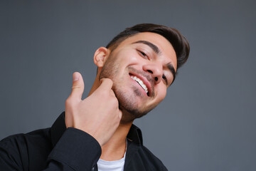 Close-up portrait of smiling handsome guy touching unshaven chin on gray background. View from below. High quality photo
