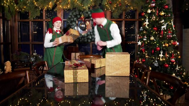 Happy elves working with Christmas presents. Elves put gift boxes on the table in the Christmas decorated room in Santa's residence.