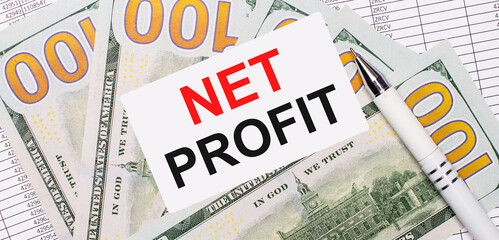 Against the background of reports and dollars - a white pen and a card with the text NET PROFIT. Business concept