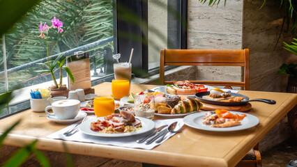 Breakfast in luxury hotel. Table full of various food from buffet in modern resort. Morning food - fresh bakery, glasses of orange juice, eggs, cold cuts and plate with tropical fruits in restaurant