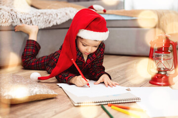 Little boy child in a santa hat writes a letter to santa claus lying on the floor.