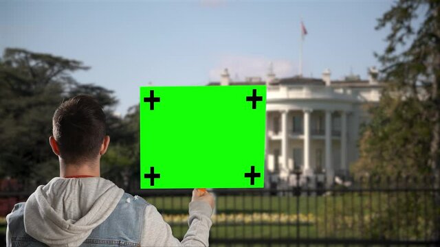 A man holds a blank green screen chroma key sign and shouts outside the White House in Washington DC.